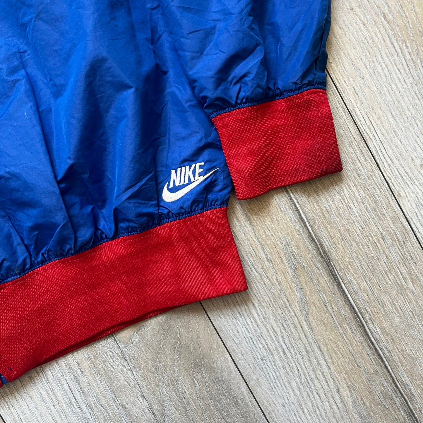 Nike UK Olympics 2008 Split Windbreaker designed by Jarrett Reynolds. Features a blue base with Union Jack-inspired red and white stripes on the front, representing Great Britain. Dual side zippers allow the jacket to be split in half and combined with other pieces from the collection, with a subtle United Kingdom flags inside the pocket.