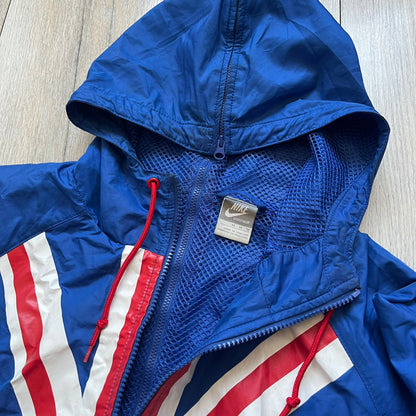 Nike UK Olympics 2008 Split Windbreaker designed by Jarrett Reynolds. Features a blue base with Union Jack-inspired red and white stripes on the front, representing Great Britain. Dual side zippers allow the jacket to be split in half and combined with other pieces from the collection, with a subtle United Kingdom flags inside the pocket.
