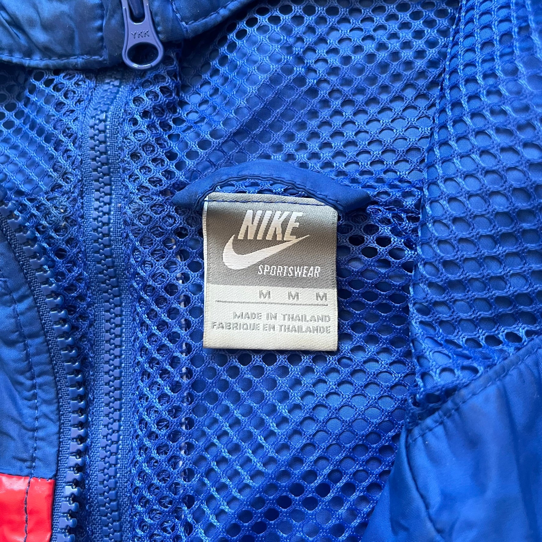 Nike UK Olympics 2008 Split Windbreaker designed by Jarrett Reynolds. Features a blue base with Union Jack-inspired red and white stripes on the front, representing Great Britain. Dual side zippers allow the jacket to be split in half and combined with other pieces from the collection, with a subtle United Kingdom flags inside the pocket.