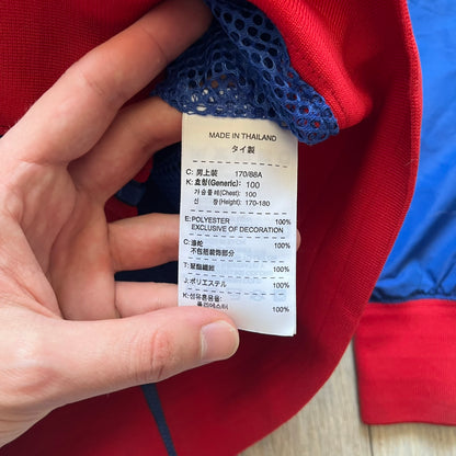 Nike UK Olympics 2008 Split Windbreaker designed by Jarrett Reynolds. Features a blue base with Union Jack-inspired red and white stripes on the front, representing Great Britain. Dual side zippers allow the jacket to be split in half and combined with other pieces from the collection, with a subtle United Kingdom flags inside the pocket.