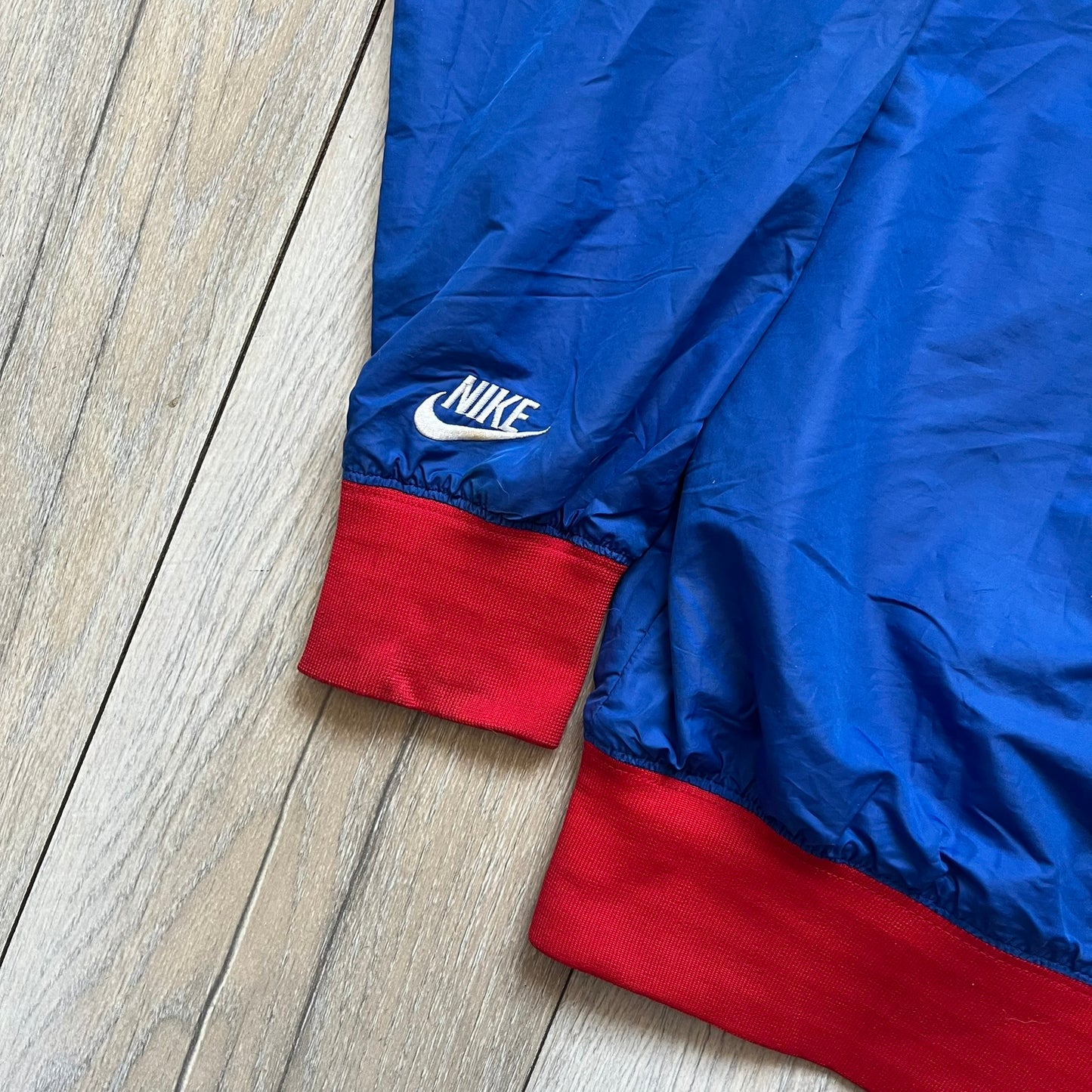 Nike UK Olympics 2008 Split Windbreaker designed by Jarrett Reynolds. Features a blue base with Union Jack-inspired red and white stripes on the front, representing Great Britain. Dual side zippers allow the jacket to be split in half and combined with other pieces from the collection, with a subtle United Kingdom flags inside the pocket.