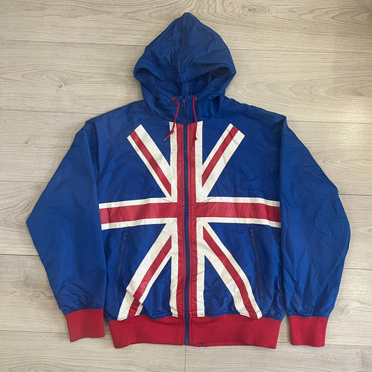 Nike UK Olympics 2008 Split Windbreaker designed by Jarrett Reynolds. Features a blue base with Union Jack-inspired red and white stripes on the front, representing Great Britain. Dual side zippers allow the jacket to be split in half and combined with other pieces from the collection, with a subtle United Kingdom flags inside the pocket.
