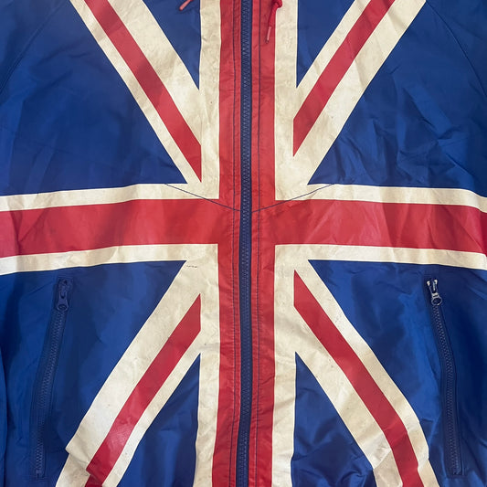 Nike UK Olympics 2008 Split Windbreaker designed by Jarrett Reynolds. Features a blue base with Union Jack-inspired red and white stripes on the front, representing Great Britain. Dual side zippers allow the jacket to be split in half and combined with other pieces from the collection, with a subtle United Kingdom flags inside the pocket.