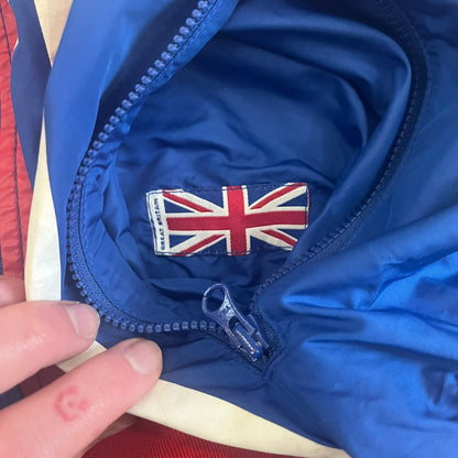 Nike UK Olympics 2008 Split Windbreaker designed by Jarrett Reynolds. Features a blue base with Union Jack-inspired red and white stripes on the front, representing Great Britain. Dual side zippers allow the jacket to be split in half and combined with other pieces from the collection, with a subtle United Kingdom flags inside the pocket.