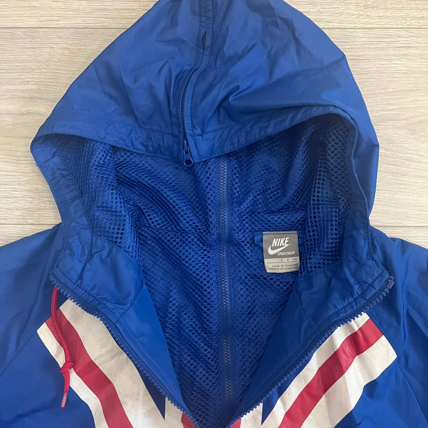 Nike UK Olympics 2008 Split Windbreaker designed by Jarrett Reynolds. Features a blue base with Union Jack-inspired red and white stripes on the front, representing Great Britain. Dual side zippers allow the jacket to be split in half and combined with other pieces from the collection, with a subtle United Kingdom flags inside the pocket.