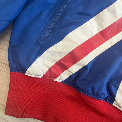 Nike UK Olympics 2008 Split Windbreaker designed by Jarrett Reynolds. Features a blue base with Union Jack-inspired red and white stripes on the front, representing Great Britain. Dual side zippers allow the jacket to be split in half and combined with other pieces from the collection, with a subtle United Kingdom flags inside the pocket.