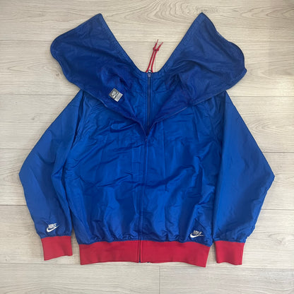 Nike UK Olympics 2008 Split Windbreaker designed by Jarrett Reynolds. Features a blue base with Union Jack-inspired red and white stripes on the front, representing Great Britain. Dual side zippers allow the jacket to be split in half and combined with other pieces from the collection, with a subtle United Kingdom flags inside the pocket.