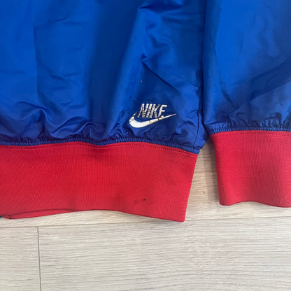 Nike UK Olympics 2008 Split Windbreaker designed by Jarrett Reynolds. Features a blue base with Union Jack-inspired red and white stripes on the front, representing Great Britain. Dual side zippers allow the jacket to be split in half and combined with other pieces from the collection, with a subtle United Kingdom flags inside the pocket.