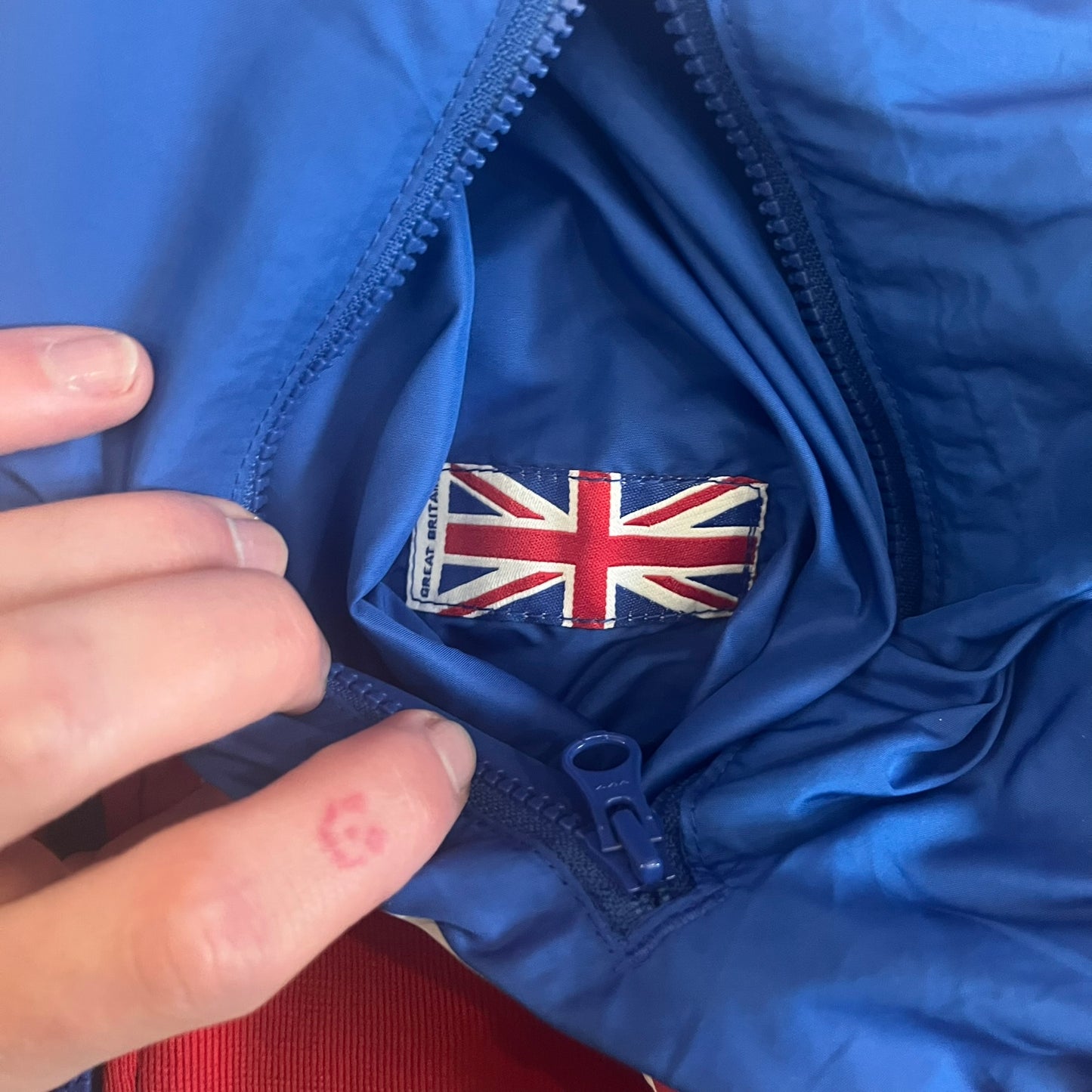 Nike UK Olympics 2008 Split Windbreaker designed by Jarrett Reynolds. Features a blue base with Union Jack-inspired red and white stripes on the front, representing Great Britain. Dual side zippers allow the jacket to be split in half and combined with other pieces from the collection, with a subtle United Kingdom flags inside the pocket.
