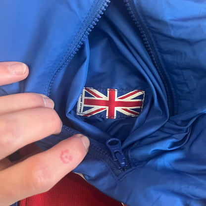 Nike UK Olympics 2008 Split Windbreaker designed by Jarrett Reynolds. Features a blue base with Union Jack-inspired red and white stripes on the front, representing Great Britain. Dual side zippers allow the jacket to be split in half and combined with other pieces from the collection, with a subtle United Kingdom flags inside the pocket.