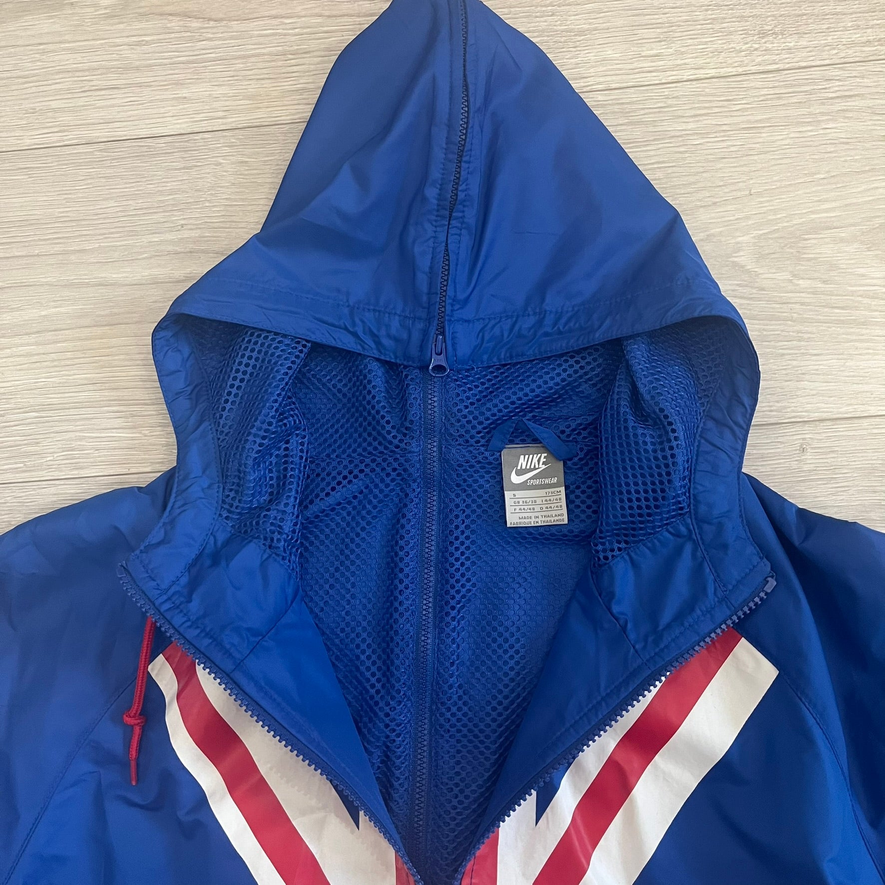 Nike UK Olympics 2008 Split Windbreaker designed by Jarrett Reynolds. Features a blue base with Union Jack-inspired red and white stripes on the front, representing Great Britain. Dual side zippers allow the jacket to be split in half and combined with other pieces from the collection, with a subtle United Kingdom flags inside the pocket.