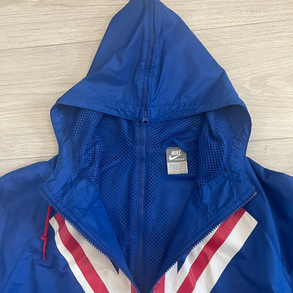 Nike UK Olympics 2008 Split Windbreaker designed by Jarrett Reynolds. Features a blue base with Union Jack-inspired red and white stripes on the front, representing Great Britain. Dual side zippers allow the jacket to be split in half and combined with other pieces from the collection, with a subtle United Kingdom flags inside the pocket.