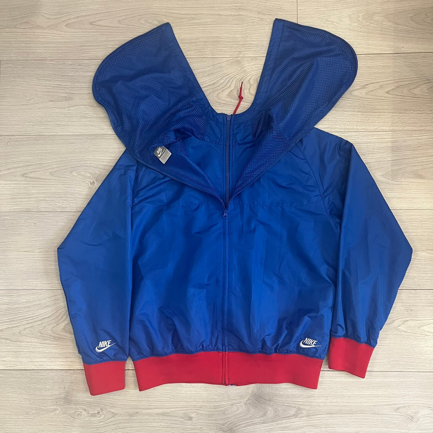 Nike UK Olympics 2008 Split Windbreaker designed by Jarrett Reynolds. Features a blue base with Union Jack-inspired red and white stripes on the front, representing Great Britain. Dual side zippers allow the jacket to be split in half and combined with other pieces from the collection, with a subtle United Kingdom flags inside the pocket.