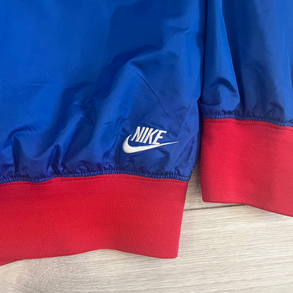 Nike UK Olympics 2008 Split Windbreaker designed by Jarrett Reynolds. Features a blue base with Union Jack-inspired red and white stripes on the front, representing Great Britain. Dual side zippers allow the jacket to be split in half and combined with other pieces from the collection, with a subtle United Kingdom flags inside the pocket.