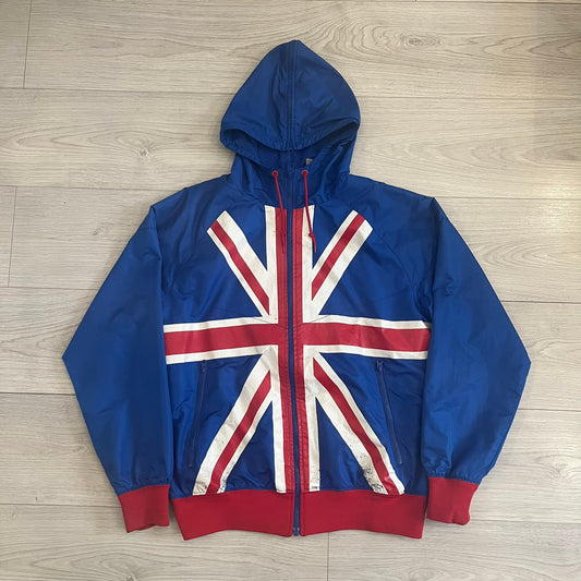 Nike UK Olympics 2008 Split Windbreaker designed by Jarrett Reynolds. Features a blue base with Union Jack-inspired red and white stripes on the front, representing Great Britain. Dual side zippers allow the jacket to be split in half and combined with other pieces from the collection, with a subtle United Kingdom flags inside the pocket.