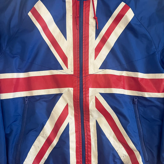 Nike UK Olympics 2008 Split Windbreaker designed by Jarrett Reynolds. Features a blue base with Union Jack-inspired red and white stripes on the front, representing Great Britain. Dual side zippers allow the jacket to be split in half and combined with other pieces from the collection, with a subtle United Kingdom flags inside the pocket.