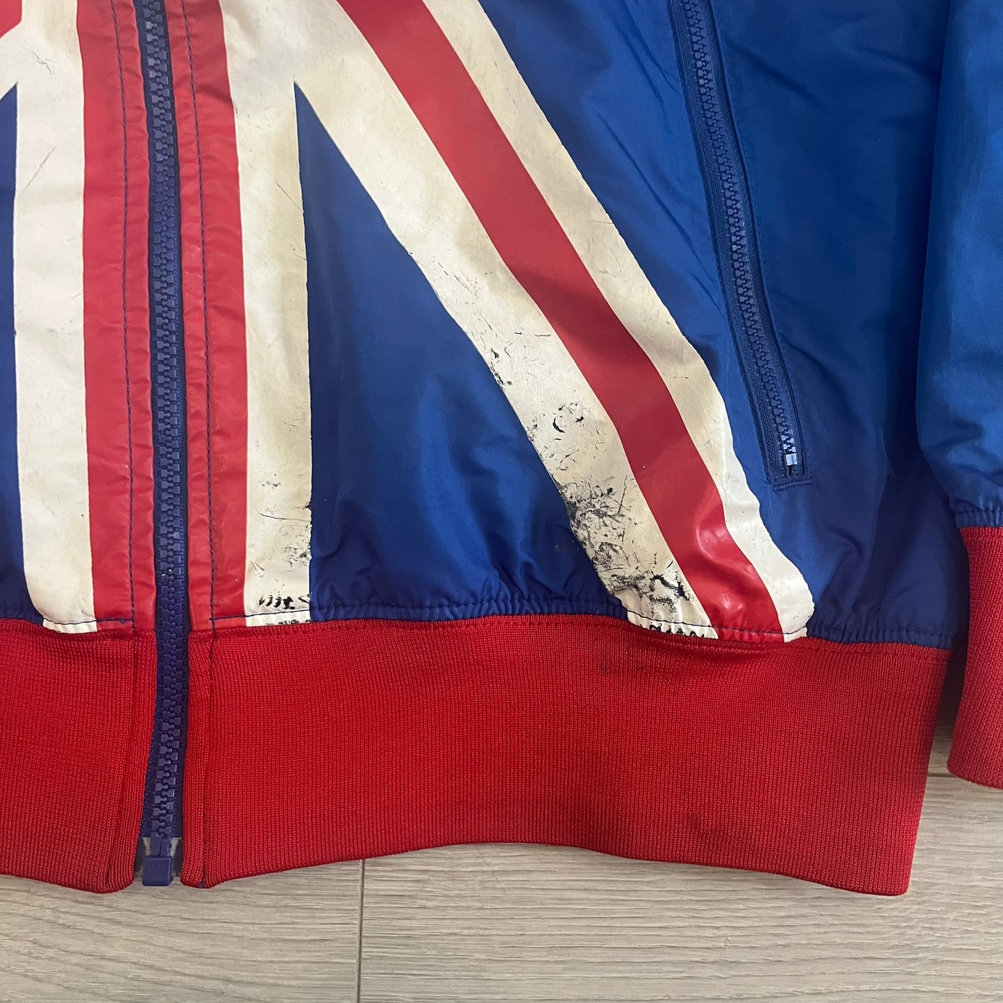 Nike UK Olympics 2008 Split Windbreaker designed by Jarrett Reynolds. Features a blue base with Union Jack-inspired red and white stripes on the front, representing Great Britain. Dual side zippers allow the jacket to be split in half and combined with other pieces from the collection, with a subtle United Kingdom flags inside the pocket.