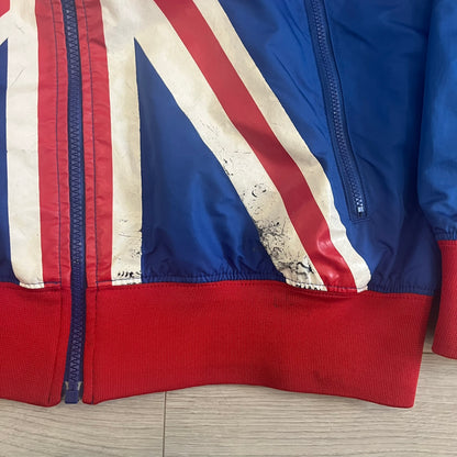 Nike UK Olympics 2008 Split Windbreaker designed by Jarrett Reynolds. Features a blue base with Union Jack-inspired red and white stripes on the front, representing Great Britain. Dual side zippers allow the jacket to be split in half and combined with other pieces from the collection, with a subtle United Kingdom flags inside the pocket.