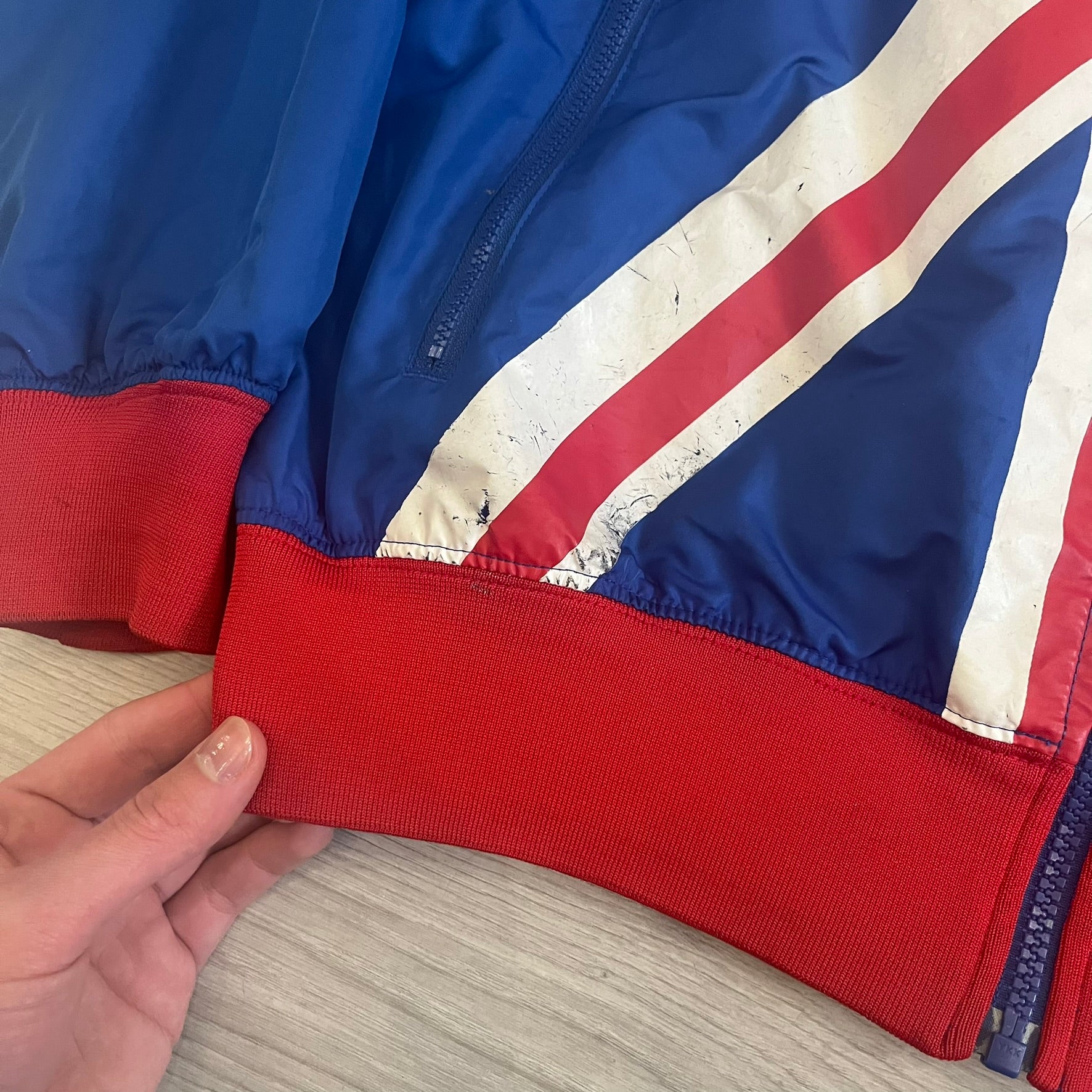 Nike UK Olympics 2008 Split Windbreaker designed by Jarrett Reynolds. Features a blue base with Union Jack-inspired red and white stripes on the front, representing Great Britain. Dual side zippers allow the jacket to be split in half and combined with other pieces from the collection, with a subtle United Kingdom flags inside the pocket.