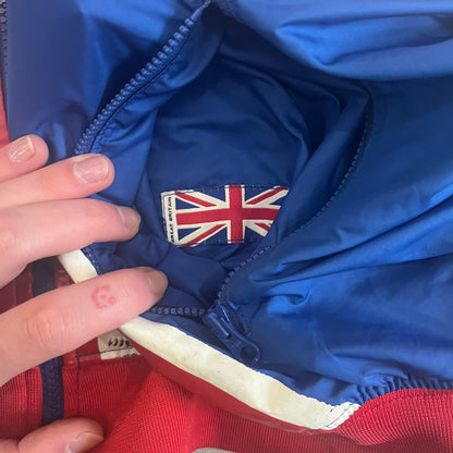 Nike UK Olympics 2008 Split Windbreaker designed by Jarrett Reynolds. Features a blue base with Union Jack-inspired red and white stripes on the front, representing Great Britain. Dual side zippers allow the jacket to be split in half and combined with other pieces from the collection, with a subtle United Kingdom flags inside the pocket.