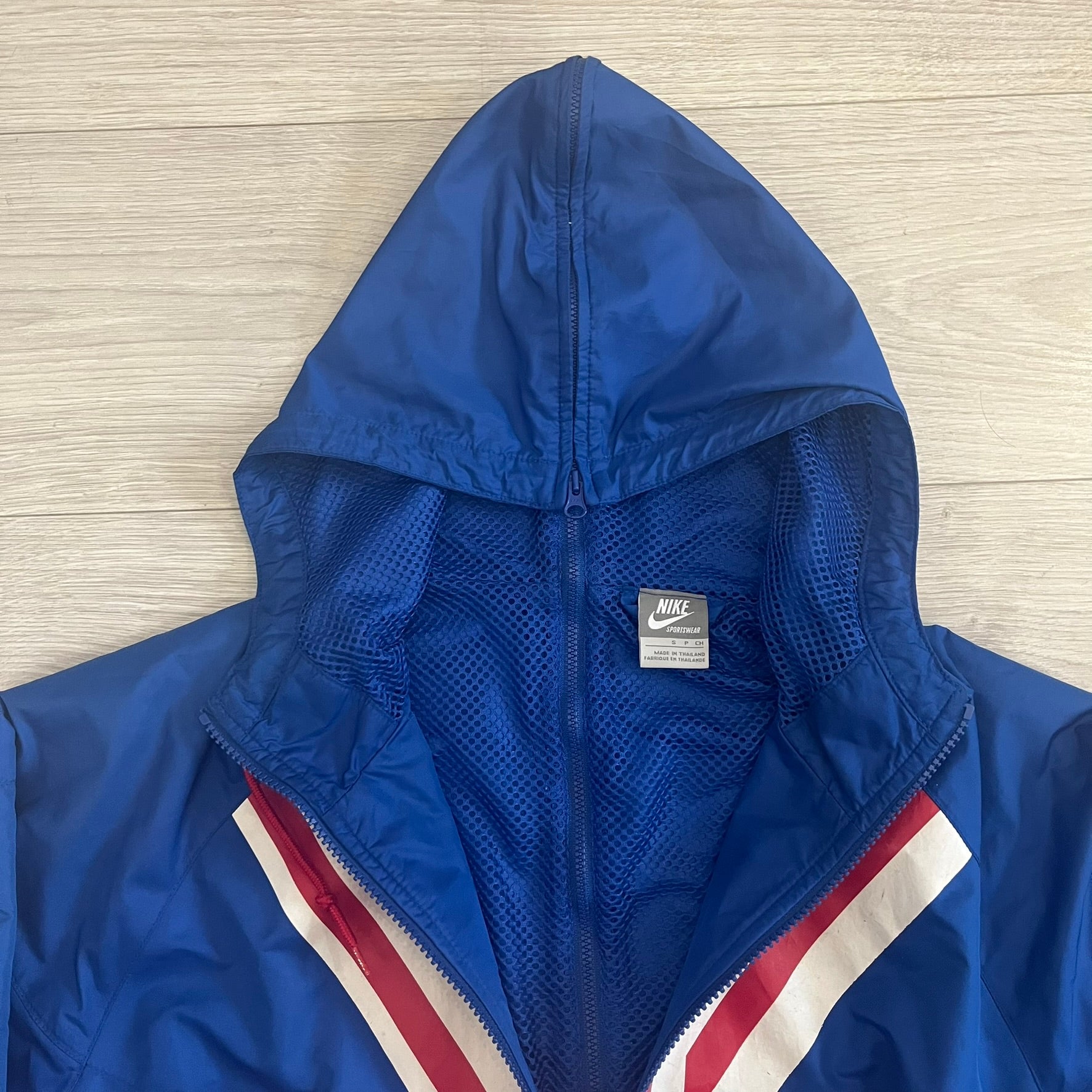 Nike UK Olympics 2008 Split Windbreaker designed by Jarrett Reynolds. Features a blue base with Union Jack-inspired red and white stripes on the front, representing Great Britain. Dual side zippers allow the jacket to be split in half and combined with other pieces from the collection, with a subtle United Kingdom flags inside the pocket.