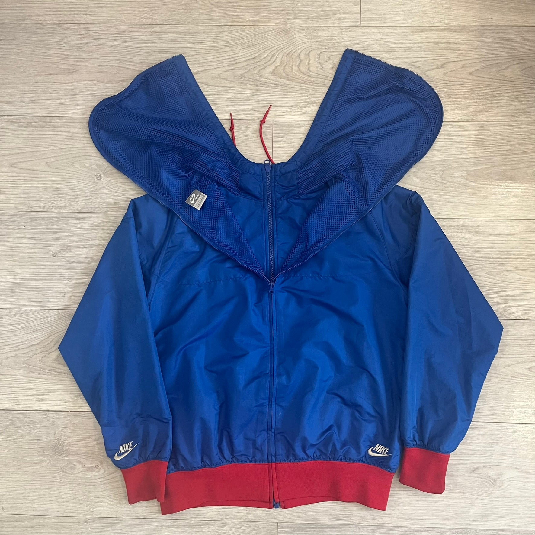 Nike UK Olympics 2008 Split Windbreaker designed by Jarrett Reynolds. Features a blue base with Union Jack-inspired red and white stripes on the front, representing Great Britain. Dual side zippers allow the jacket to be split in half and combined with other pieces from the collection, with a subtle United Kingdom flags inside the pocket.