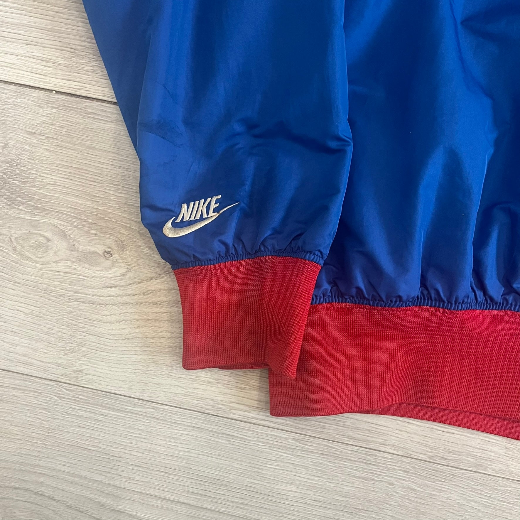 Nike UK Olympics 2008 Split Windbreaker designed by Jarrett Reynolds. Features a blue base with Union Jack-inspired red and white stripes on the front, representing Great Britain. Dual side zippers allow the jacket to be split in half and combined with other pieces from the collection, with a subtle United Kingdom flags inside the pocket.