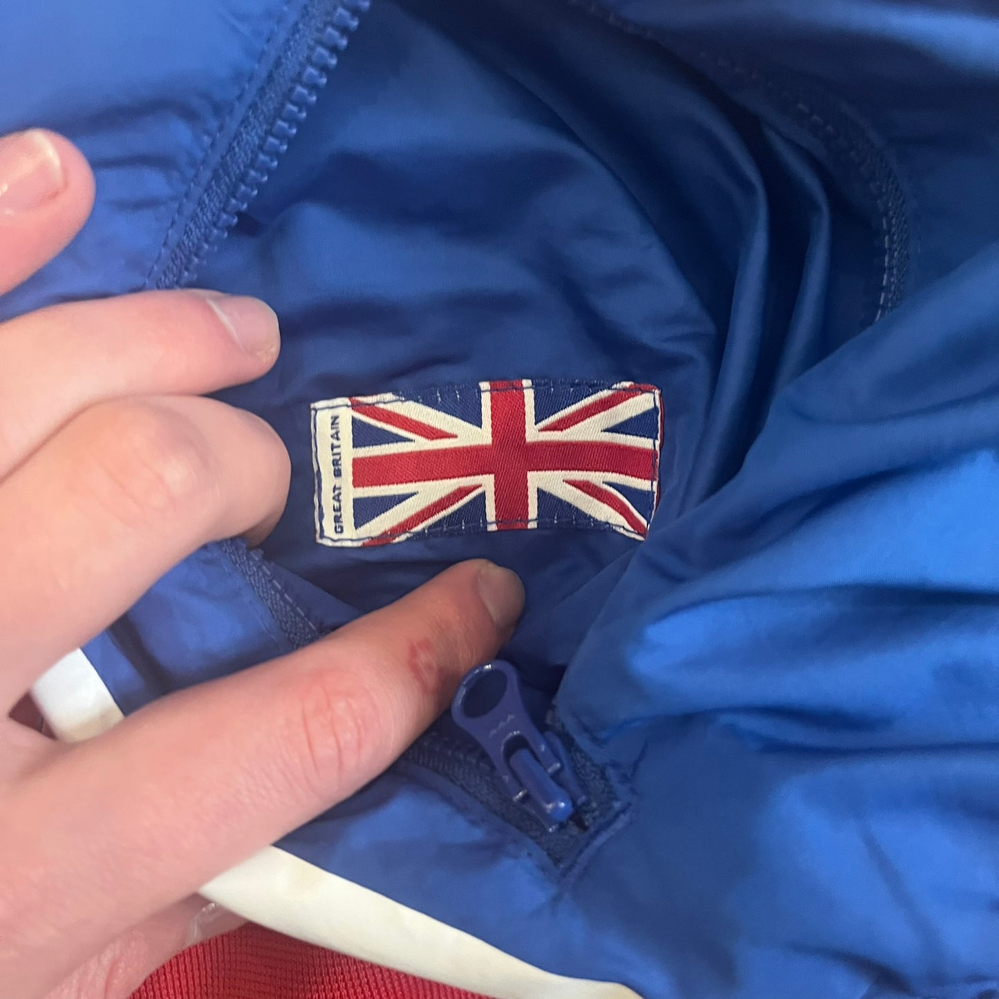 Nike UK Olympics 2008 Split Windbreaker designed by Jarrett Reynolds. Features a blue base with Union Jack-inspired red and white stripes on the front, representing Great Britain. Dual side zippers allow the jacket to be split in half and combined with other pieces from the collection, with a subtle United Kingdom flags inside the pocket.