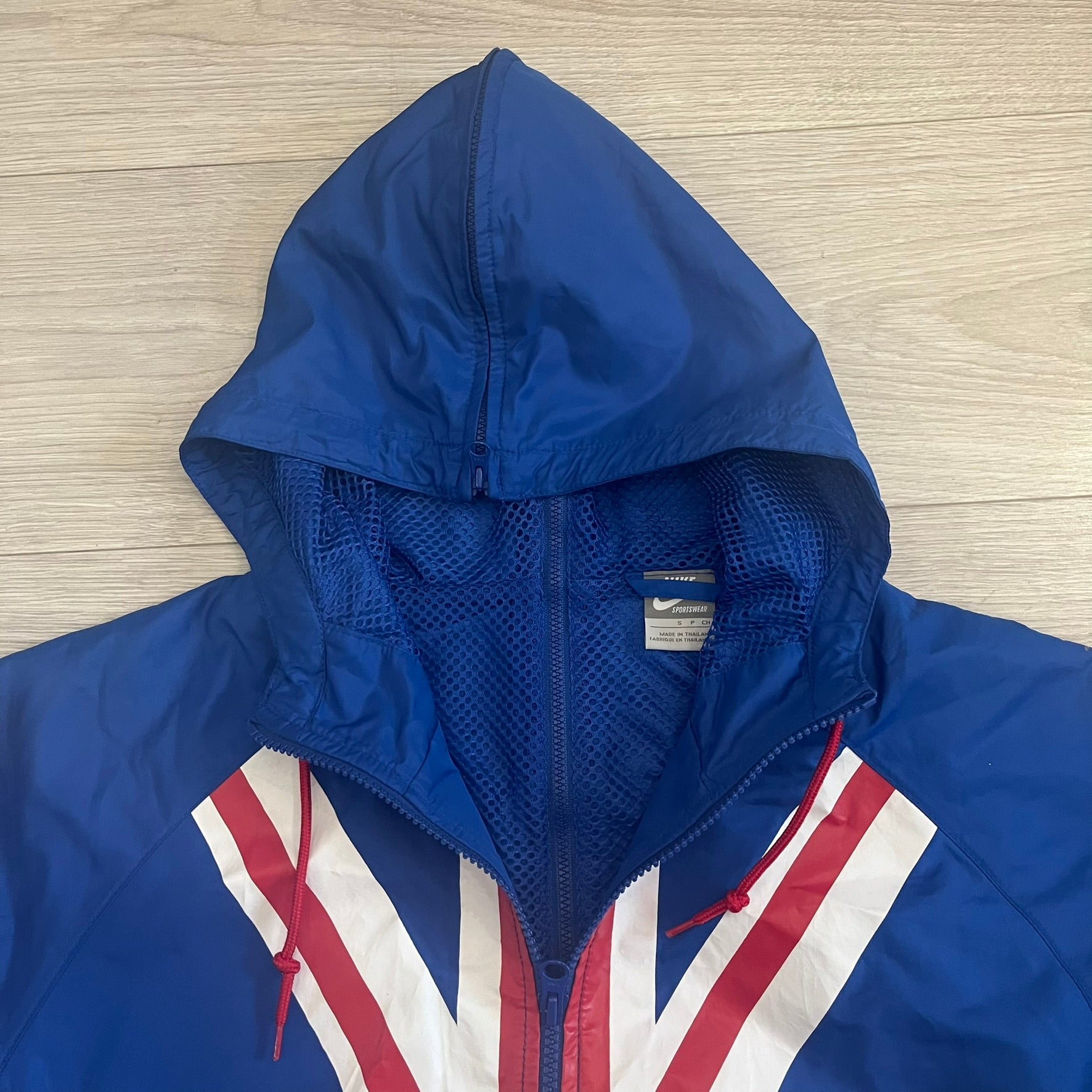 Nike UK Olympics 2008 Split Windbreaker designed by Jarrett Reynolds. Features a blue base with Union Jack-inspired red and white stripes on the front, representing Great Britain. Dual side zippers allow the jacket to be split in half and combined with other pieces from the collection, with a subtle United Kingdom flags inside the pocket.