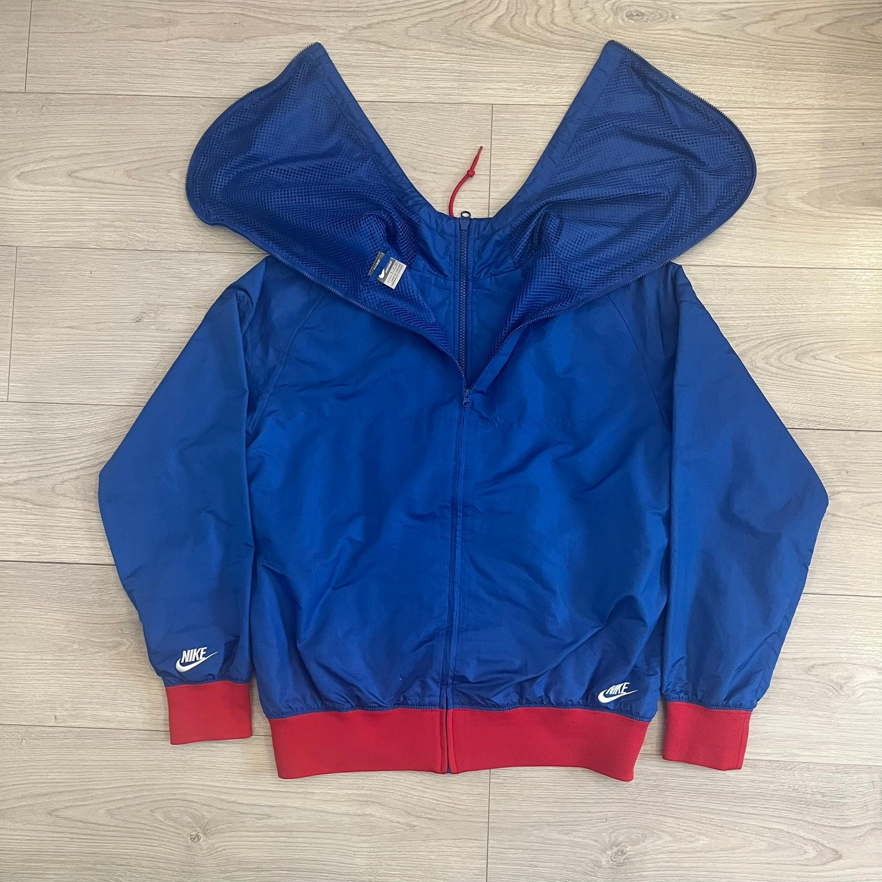 Nike UK Olympics 2008 Split Windbreaker designed by Jarrett Reynolds. Features a blue base with Union Jack-inspired red and white stripes on the front, representing Great Britain. Dual side zippers allow the jacket to be split in half and combined with other pieces from the collection, with a subtle United Kingdom flags inside the pocket.