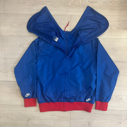 Nike UK Olympics 2008 Split Windbreaker designed by Jarrett Reynolds. Features a blue base with Union Jack-inspired red and white stripes on the front, representing Great Britain. Dual side zippers allow the jacket to be split in half and combined with other pieces from the collection, with a subtle United Kingdom flags inside the pocket.