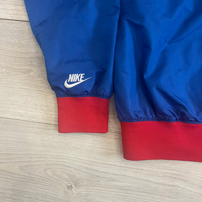 Nike UK Olympics 2008 Split Windbreaker designed by Jarrett Reynolds. Features a blue base with Union Jack-inspired red and white stripes on the front, representing Great Britain. Dual side zippers allow the jacket to be split in half and combined with other pieces from the collection, with a subtle United Kingdom flags inside the pocket.