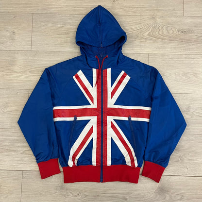 Nike UK Olympics 2008 Split Windbreaker designed by Jarrett Reynolds. Features a blue base with Union Jack-inspired red and white stripes on the front, representing Great Britain. Dual side zippers allow the jacket to be split in half and combined with other pieces from the collection, with a subtle United Kingdom flags inside the pocket.