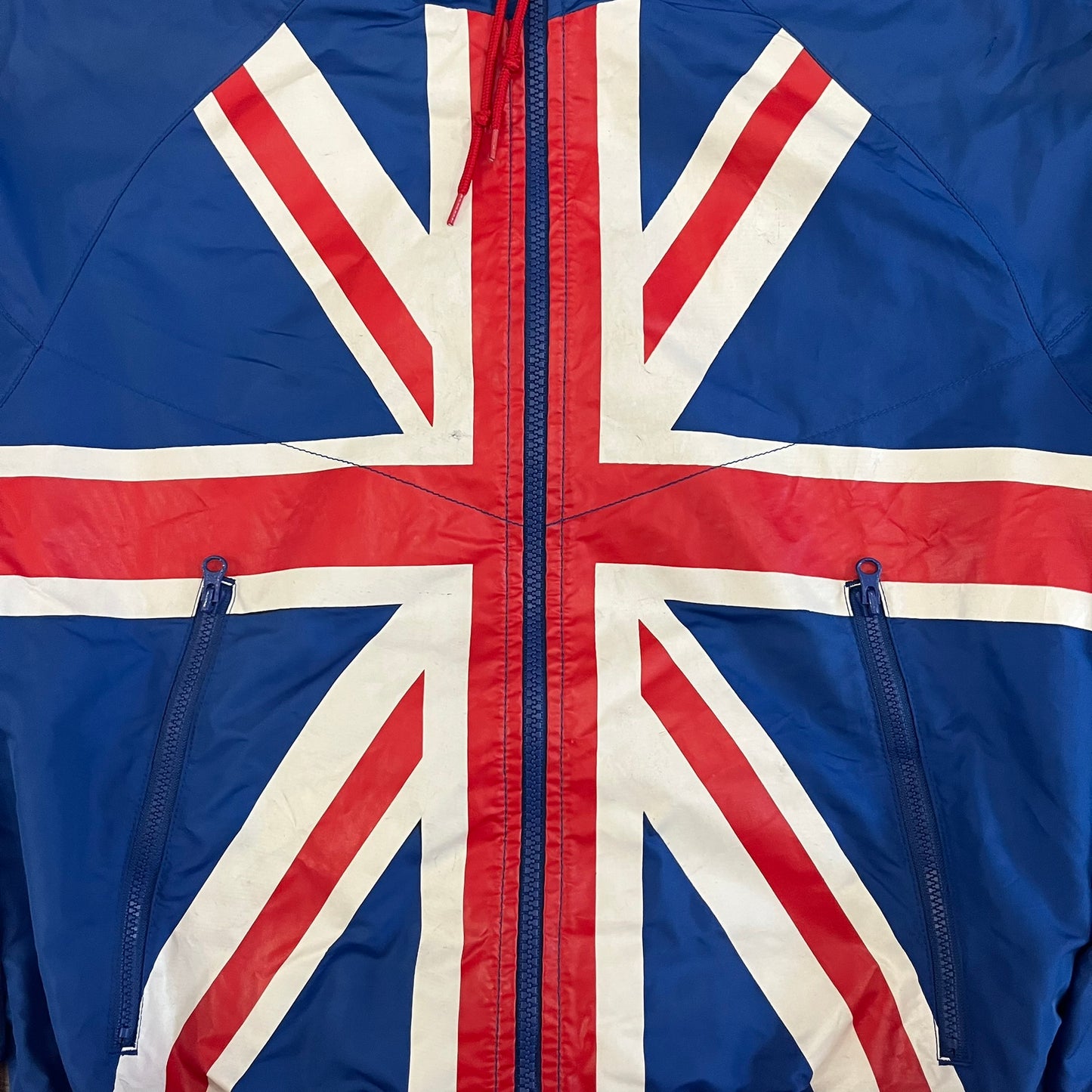 Nike UK Olympics 2008 Split Windbreaker designed by Jarrett Reynolds. Features a blue base with Union Jack-inspired red and white stripes on the front, representing Great Britain. Dual side zippers allow the jacket to be split in half and combined with other pieces from the collection, with a subtle United Kingdom flags inside the pocket.