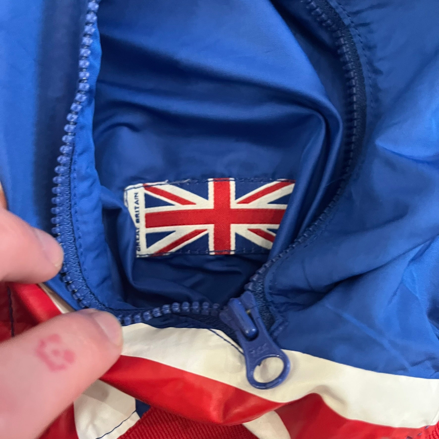 Nike UK Olympics 2008 Split Windbreaker designed by Jarrett Reynolds. Features a blue base with Union Jack-inspired red and white stripes on the front, representing Great Britain. Dual side zippers allow the jacket to be split in half and combined with other pieces from the collection, with a subtle United Kingdom flags inside the pocket.