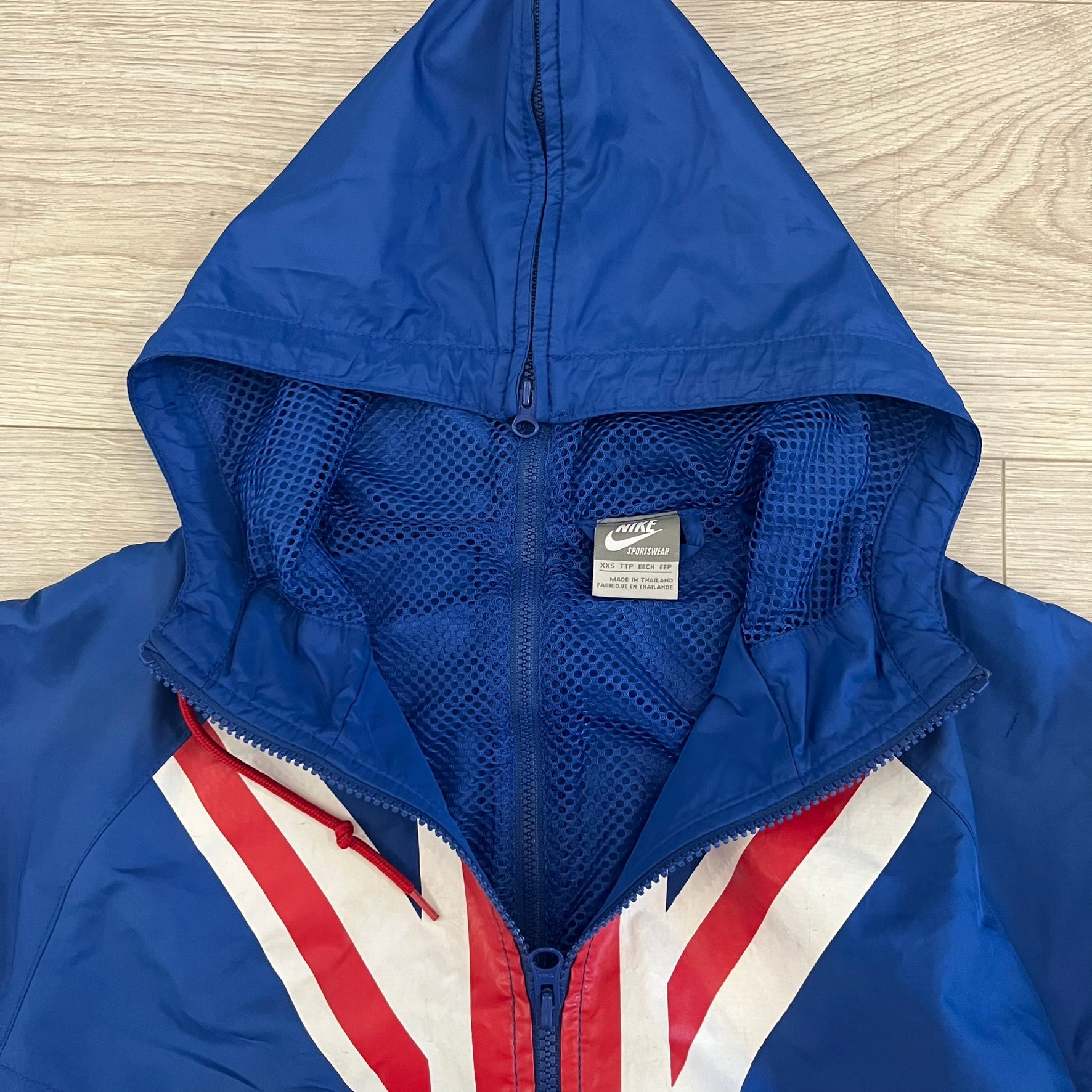 Nike UK Olympics 2008 Split Windbreaker designed by Jarrett Reynolds. Features a blue base with Union Jack-inspired red and white stripes on the front, representing Great Britain. Dual side zippers allow the jacket to be split in half and combined with other pieces from the collection, with a subtle United Kingdom flags inside the pocket.
