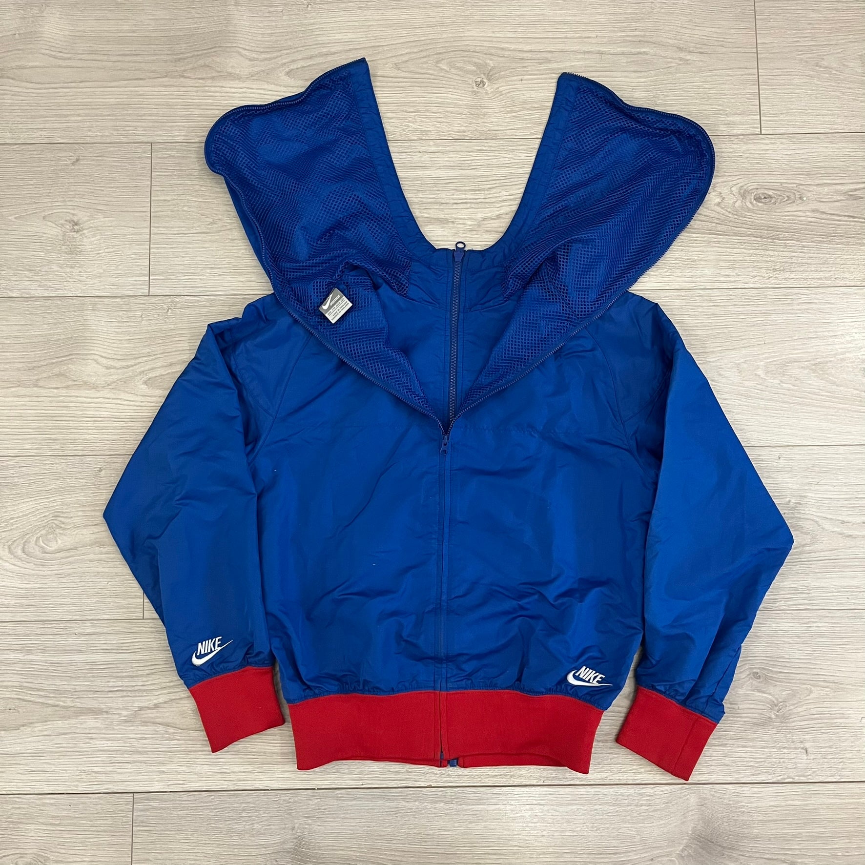 Nike UK Olympics 2008 Split Windbreaker designed by Jarrett Reynolds. Features a blue base with Union Jack-inspired red and white stripes on the front, representing Great Britain. Dual side zippers allow the jacket to be split in half and combined with other pieces from the collection, with a subtle United Kingdom flags inside the pocket.