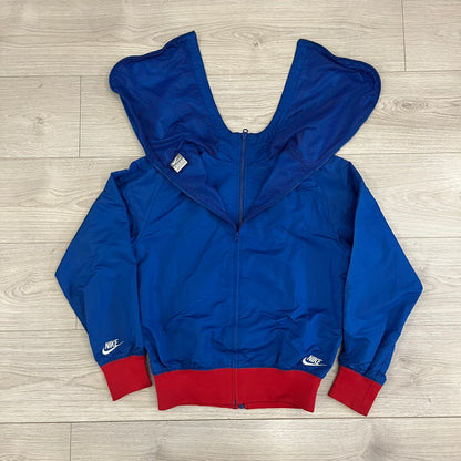 Nike UK Olympics 2008 Split Windbreaker designed by Jarrett Reynolds. Features a blue base with Union Jack-inspired red and white stripes on the front, representing Great Britain. Dual side zippers allow the jacket to be split in half and combined with other pieces from the collection, with a subtle United Kingdom flags inside the pocket.