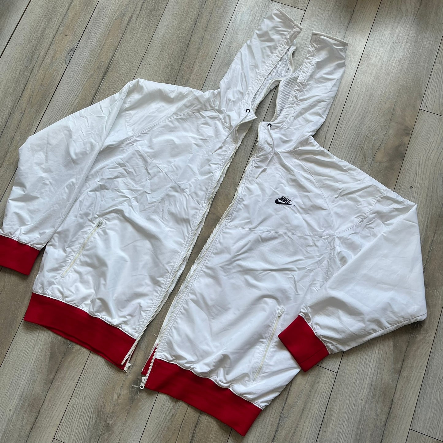 Nike United States (USA) Olympics Split Windbreaker from 2008, created by designer Jarrett Reynolds. Crafted in white, with red hems. Small Nike black embroidery on the chest and back. The upper half of the jacket have slightly visible stars all over. This innovative jacket can be zipped apart on both sides and merged with other compatible models. Hidden inside, a small USA flags accent completes the concept.