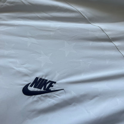 Nike United States (USA) Olympics Split Windbreaker from 2008, created by designer Jarrett Reynolds. Crafted in white, with red hems. Small Nike black embroidery on the chest and back. The upper half of the jacket have slightly visible stars all over. This innovative jacket can be zipped apart on both sides and merged with other compatible models. Hidden inside, a small USA flags accent completes the concept.