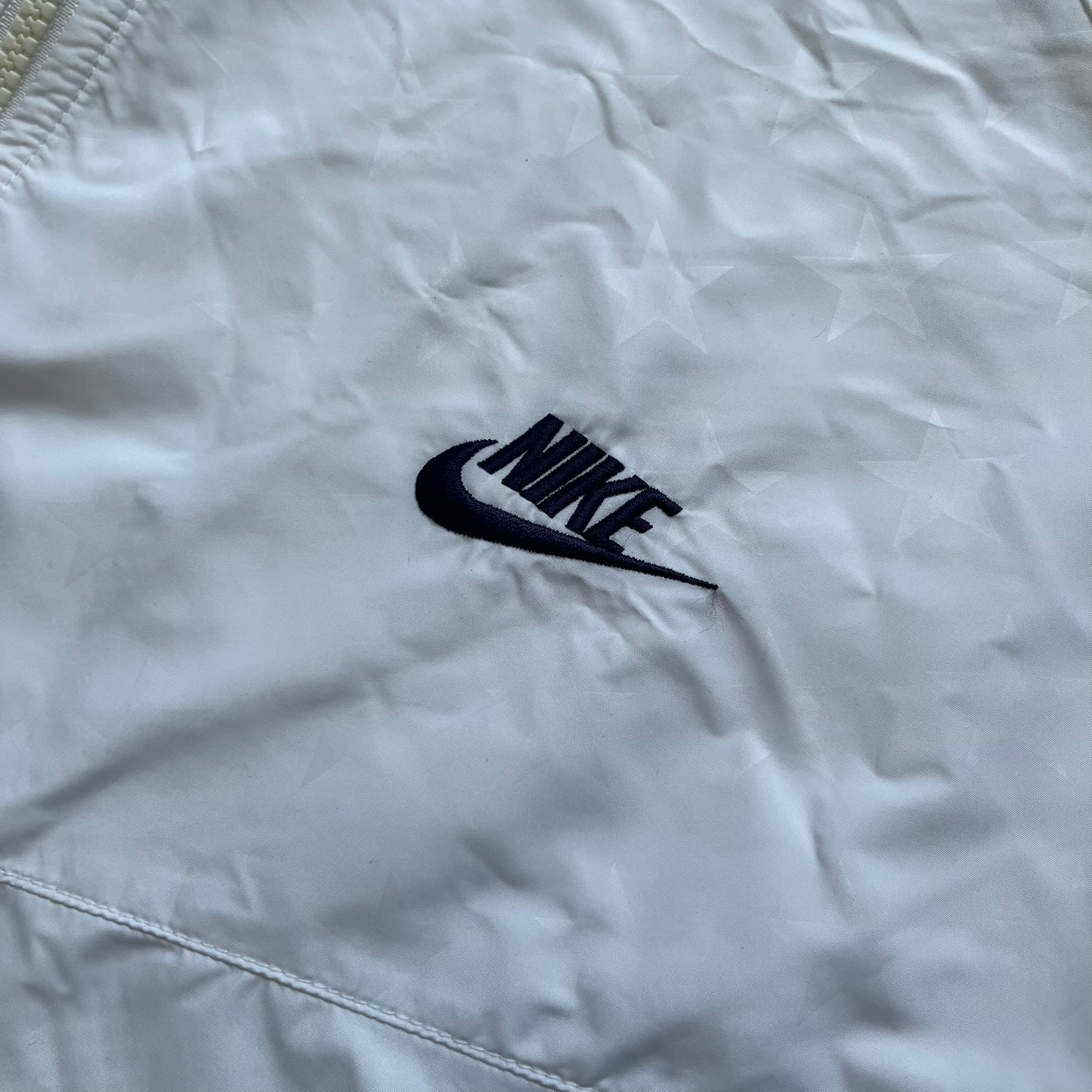 Nike United States (USA) Olympics Split Windbreaker from 2008, created by designer Jarrett Reynolds. Crafted in white, with red hems. Small Nike black embroidery on the chest and back. The upper half of the jacket have slightly visible stars all over. This innovative jacket can be zipped apart on both sides and merged with other compatible models. Hidden inside, a small USA flags accent completes the concept.