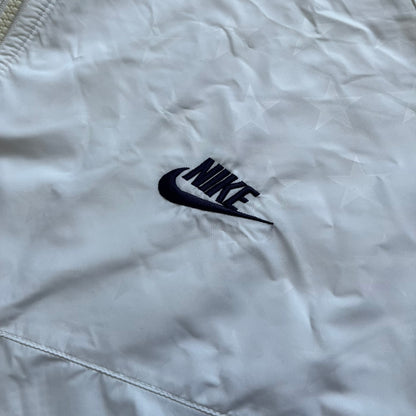 Nike United States (USA) Olympics Split Windbreaker from 2008, created by designer Jarrett Reynolds. Crafted in white, with red hems. Small Nike black embroidery on the chest and back. The upper half of the jacket have slightly visible stars all over. This innovative jacket can be zipped apart on both sides and merged with other compatible models. Hidden inside, a small USA flags accent completes the concept.