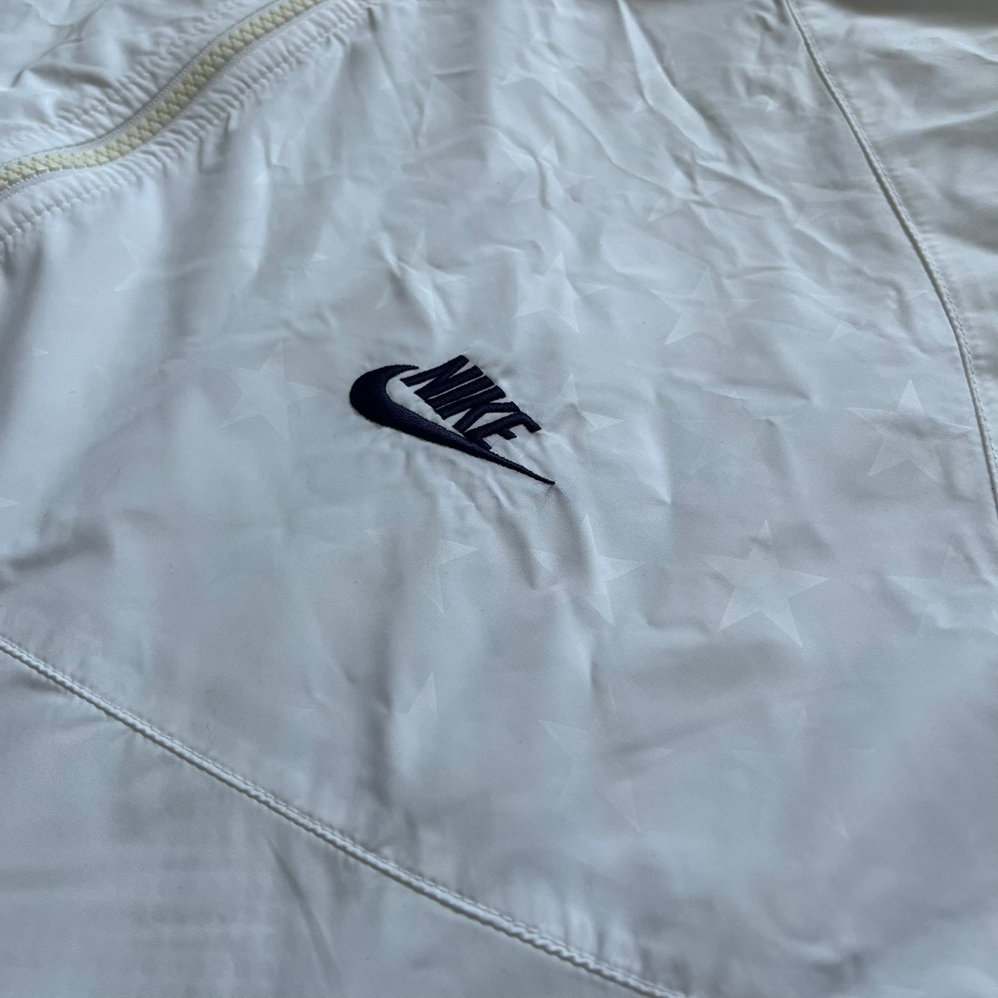 Nike United States (USA) Olympics Split Windbreaker from 2008, created by designer Jarrett Reynolds. Crafted in white, with red hems. Small Nike black embroidery on the chest and back. The upper half of the jacket have slightly visible stars all over. This innovative jacket can be zipped apart on both sides and merged with other compatible models. Hidden inside, a small USA flags accent completes the concept.