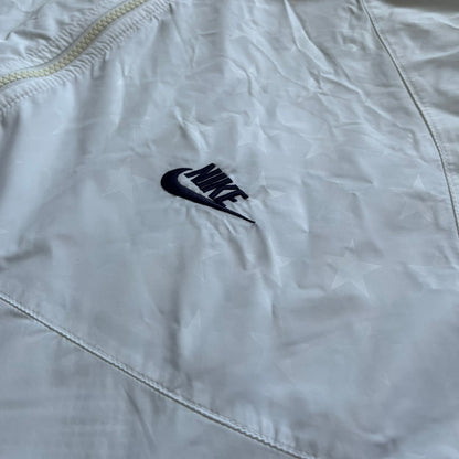 Nike United States (USA) Olympics Split Windbreaker from 2008, created by designer Jarrett Reynolds. Crafted in white, with red hems. Small Nike black embroidery on the chest and back. The upper half of the jacket have slightly visible stars all over. This innovative jacket can be zipped apart on both sides and merged with other compatible models. Hidden inside, a small USA flags accent completes the concept.