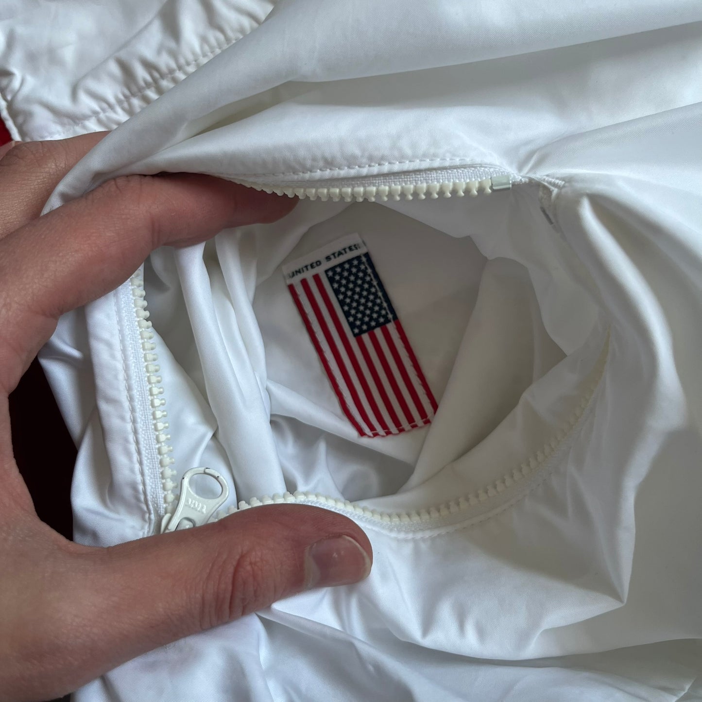 Nike United States (USA) Olympics Split Windbreaker from 2008, created by designer Jarrett Reynolds. Crafted in white, with red hems. Small Nike black embroidery on the chest and back. The upper half of the jacket have slightly visible stars all over. This innovative jacket can be zipped apart on both sides and merged with other compatible models. Hidden inside, a small USA flags accent completes the concept.