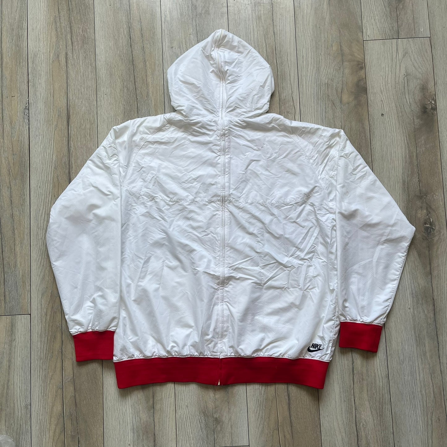 Nike United States (USA) Olympics Split Windbreaker from 2008, created by designer Jarrett Reynolds. Crafted in white, with red hems. Small Nike black embroidery on the chest and back. The upper half of the jacket have slightly visible stars all over. This innovative jacket can be zipped apart on both sides and merged with other compatible models. Hidden inside, a small USA flags accent completes the concept.
