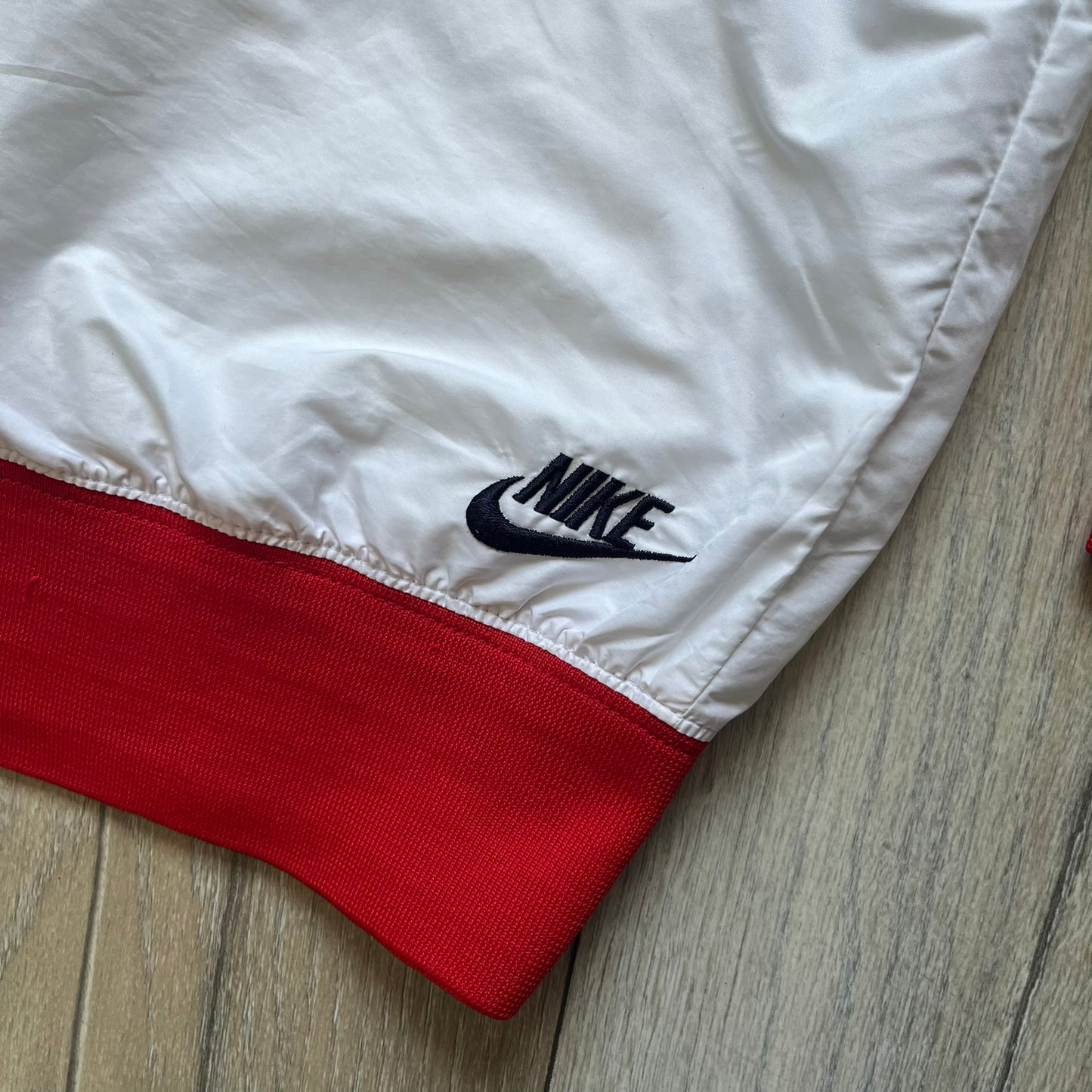 Nike United States (USA) Olympics Split Windbreaker from 2008, created by designer Jarrett Reynolds. Crafted in white, with red hems. Small Nike black embroidery on the chest and back. The upper half of the jacket have slightly visible stars all over. This innovative jacket can be zipped apart on both sides and merged with other compatible models. Hidden inside, a small USA flags accent completes the concept.