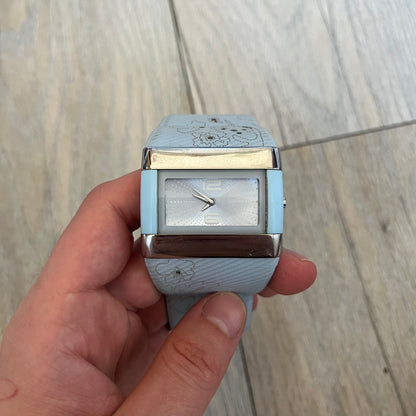 Nike WC0024-624 Merge Attract Baby Blue Digital Watch is a digital wristwatch featuring a silver-tone stainless steel case with a analog display. The straps are baby blue with engraved floral pattern graphics on the outer side and a beige inner lining, made from a combination of leather, plastic, and rubber materials. The dial is metallic baby blue with small dots pattern.
