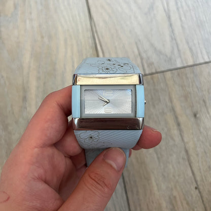Nike WC0024-624 Merge Attract Baby Blue Digital Watch is a digital wristwatch featuring a silver-tone stainless steel case with a analog display. The straps are baby blue with engraved floral pattern graphics on the outer side and a beige inner lining, made from a combination of leather, plastic, and rubber materials. The dial is metallic baby blue with small dots pattern.