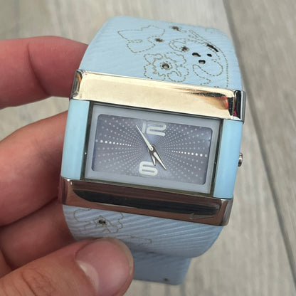 Nike WC0024-624 Merge Attract Baby Blue Digital Watch is a digital wristwatch featuring a silver-tone stainless steel case with a analog display. The straps are baby blue with engraved floral pattern graphics on the outer side and a beige inner lining, made from a combination of leather, plastic, and rubber materials. The dial is metallic baby blue with small dots pattern.